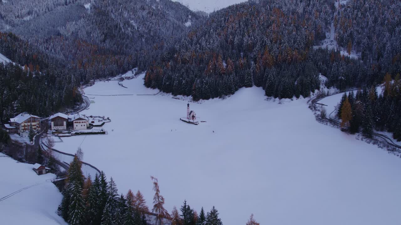 Dolomiti innevate e la Chiesa di San Giovanni che risplende al crepuscolo, Val di Funes, Italia