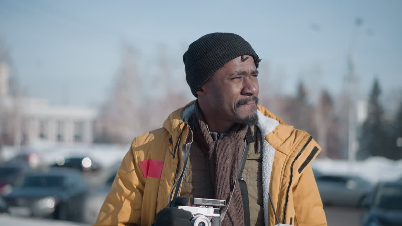 close up press photographer sipping morning coffee in winter chill, holding camera with other hand while scanning snowy city streets under bright sun, visible breath rising in crisp air around him