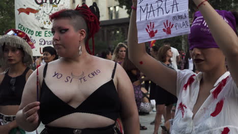 activists sisterhood manifests during women’s day public march with flags and signs. they represent blood and injustice with red body paint