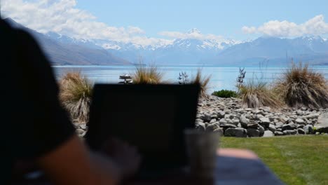 person typing on computer outside with stunning views of mount cook and lake pukaki