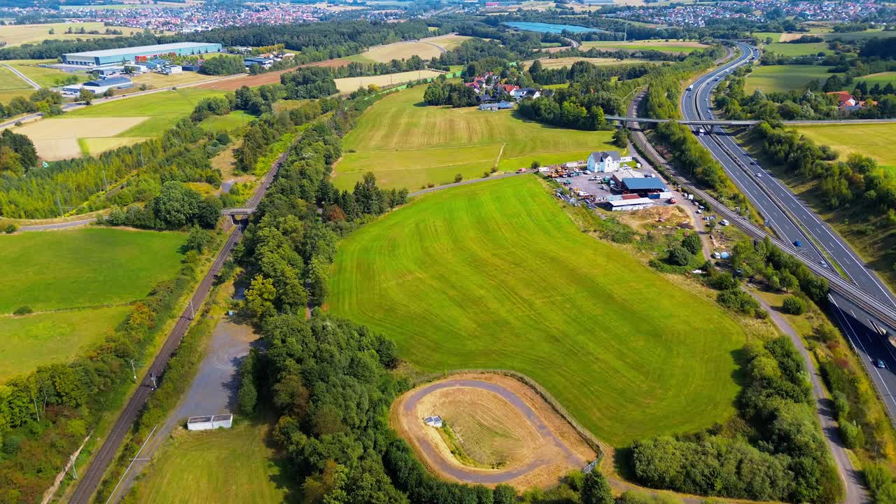 Aerial view of farmland, railway, and highway cutting through rural landscape with towns in the distance