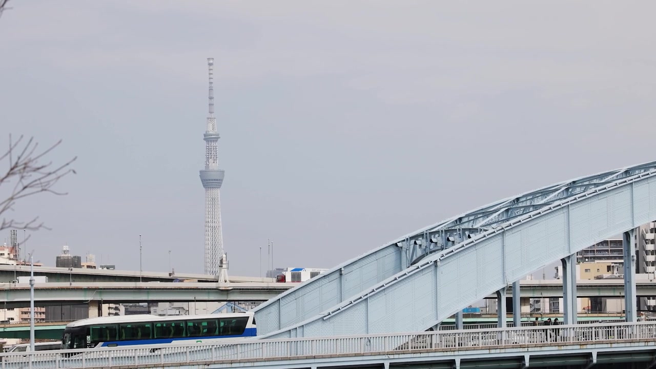 Statische Weitwinkelaufnahme des Tokyo Skytree hinter einer Stahlbrücke mit fließendem Verkehr in Tokio