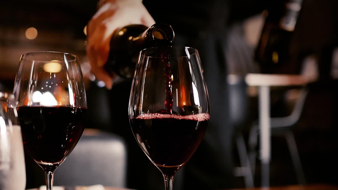 Un cameriere versa vino rosso da una bottiglia in un bicchiere in un ristorante a luci soffuse