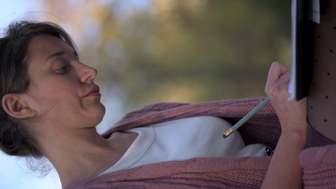 Woman writing on paper on a bench in the park on a sunny day. Vertical