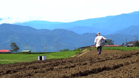 farmer tilling soil in mountainous rural landscape