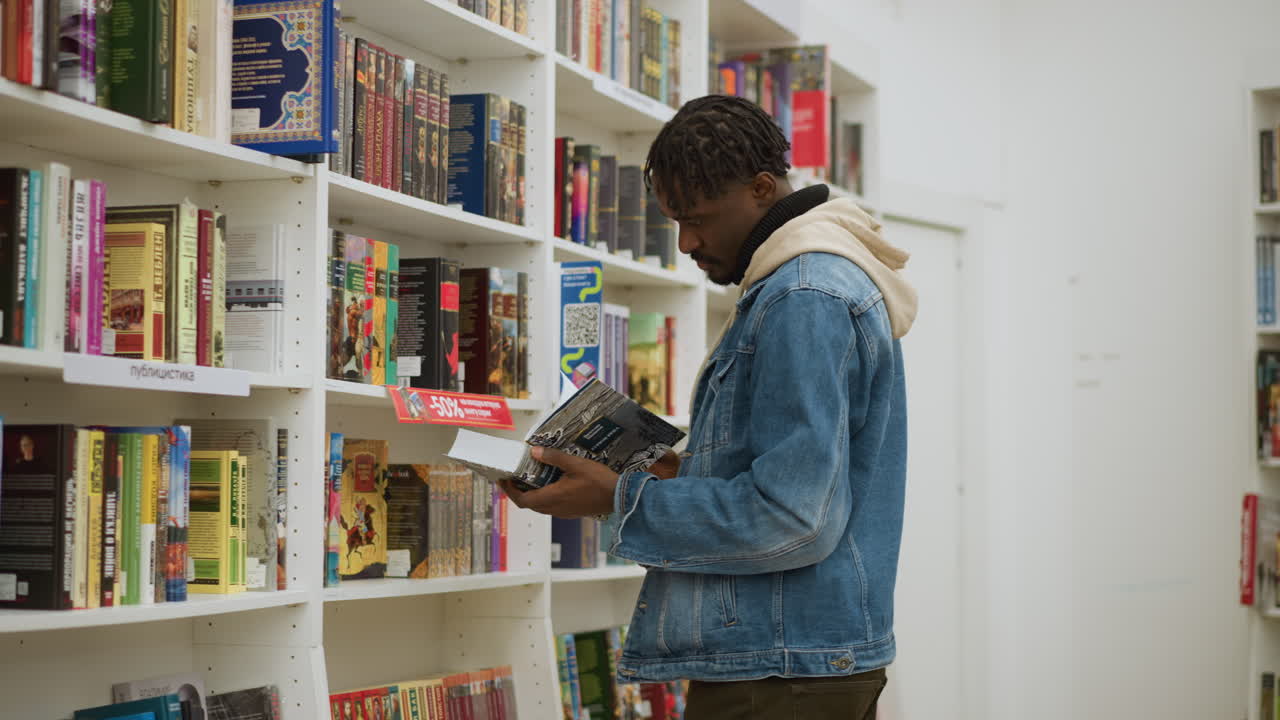 Student in casual clothing standing in front of library shelves, holding a book, carefully inspecting it, surrounded by rows of colorful books in a modern, organized, and peaceful study space