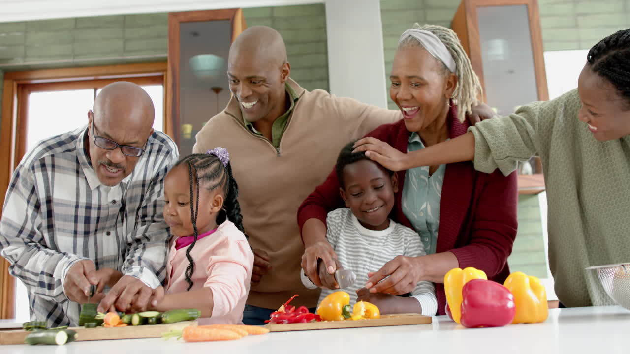 Glad afroamerikansk flergenerationsfamilie, der hakker grøntsager i køkkenet, i slowmotion.