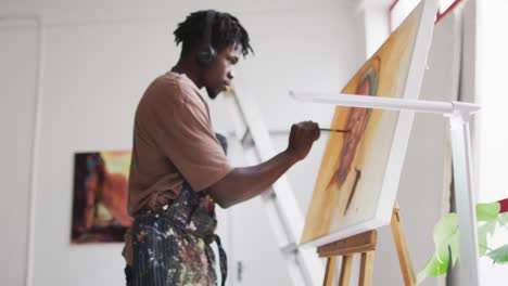 African-american-male-artist-wearing-headphones-painting-on-canvas-at-art-studio