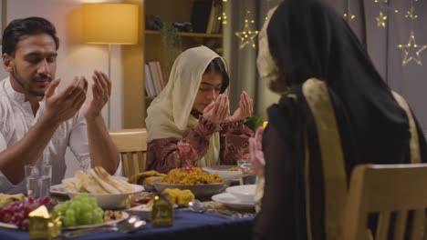 muslim muslim family sitting around table at home praying before eating meal to celebrate eid