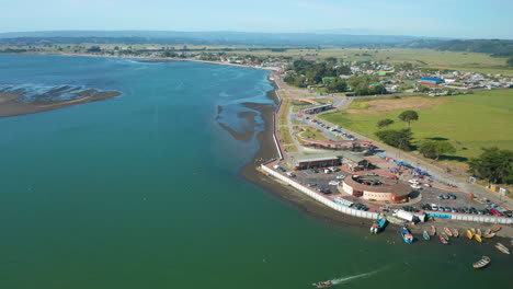 Aerial-dolly-shot-looking-over-the-coastal-line-of-Puerto-Saavedra,-Chile,-blue-water-and-bright-blue-sky