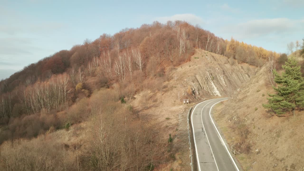 una vista aérea ascendente de un dron de un coche conduciendo por una carretera sinuosa que atraviesa un cañón a finales de otoño