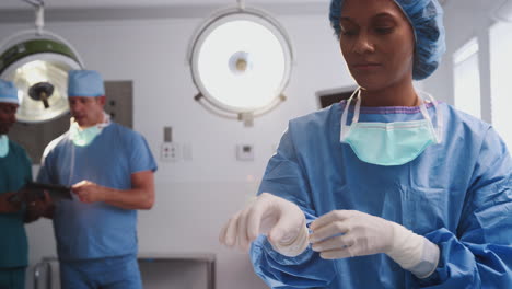 female surgeon wearing scrubs putting on latex gloves in hospital operating theater