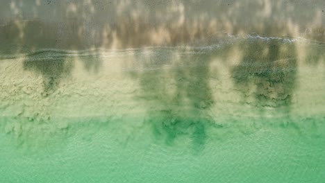 Bird's-eye-view-of-ocean-waves-crashing-against-an-empty-sand-beach-from-above