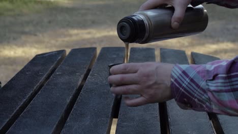 woman pouring drink from flask at wooden picnic table close up shot