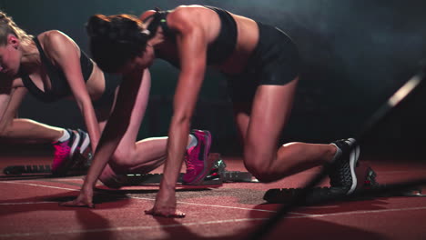 tres chicas deportivas con ropa negra del atleta por la noche en la cinta de correr comenzarán la carrera a la distancia de sprint desde la posición sentada.