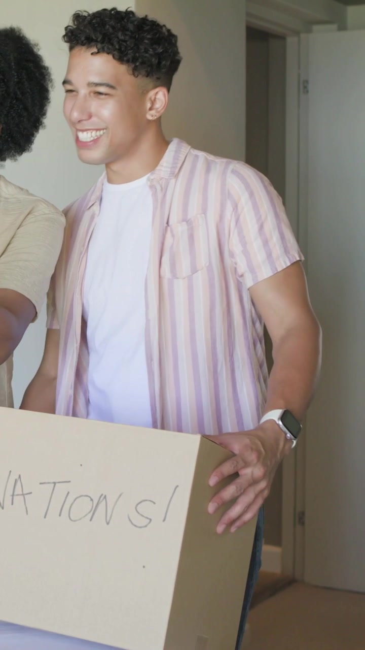 Vertical video: Picking pink top, man in striped shirt packing and carrying donations box at home