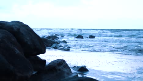 Vista-De-Cangrejos-De-Pequeñas-Olas-Que-Chocan-Contra-Rocas-Oscuras-Y-Resbaladizas-En-Una-Tarde-Fría-Con-La-Puesta-De-Sol-Derramando-Un-Tinte-Azul-Por-Todas-Partes