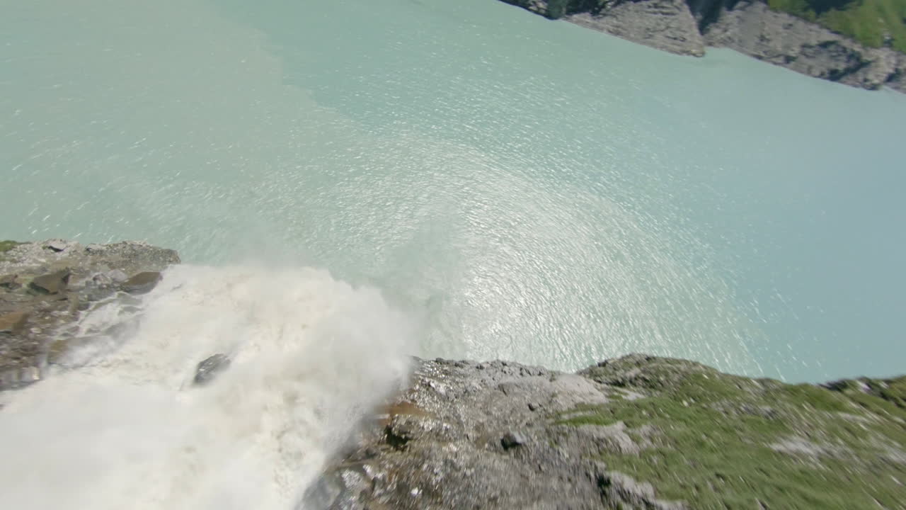 Stunning FPV and drone shots soaring through the Swiss Alps, capturing the Mauvoisin Dam and its majestic waterfall on a clear, sunny summer day.