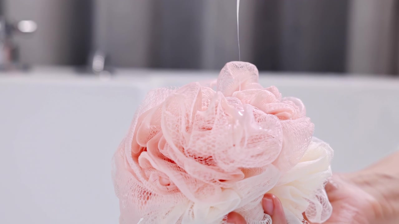 Unrecognizable young woman hand pours shampoo shower gel douche into bath mesh sponge, cleanliness bodycare, self-hygiene and healthcare using liquid soap product for cleaning body concept