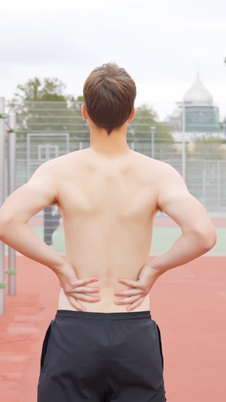 Rear view of shirtless man stretching after workout session on outdoor running track under daylight
