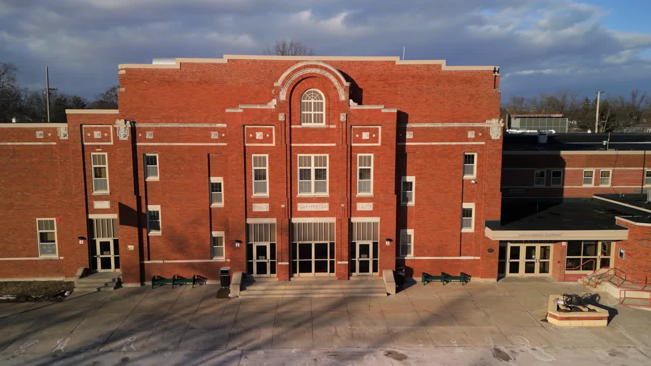 Old brick school building in suburban area under clear blue sky with wide front facade, aerial establishing orbit