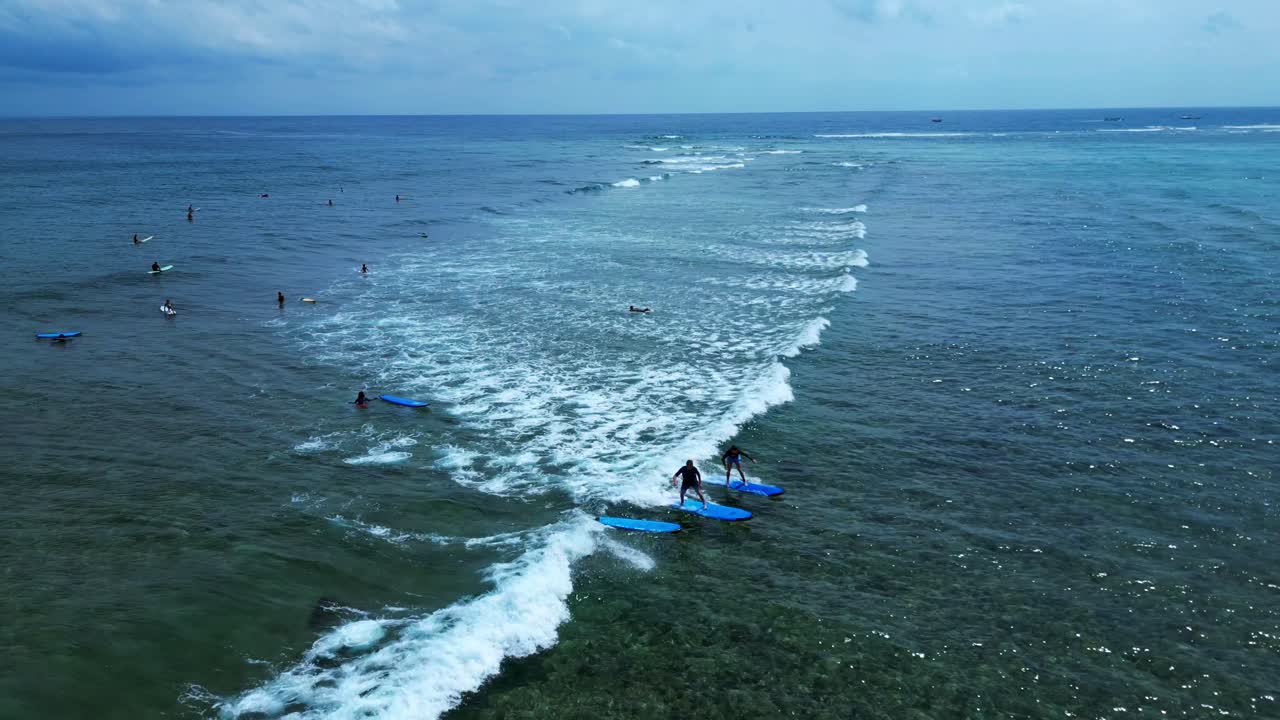 Giovani che imparano e praticano le abilità di surf su piccole onde nel mare tropicale chiaro e poco profondo. Spettacolare ripresa aerea con drone dall'alto.