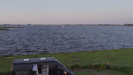 Camper-van-parked-next-to-lake-the-Fluessen-Friesland-with-sail-boat-on-lake,-aerial