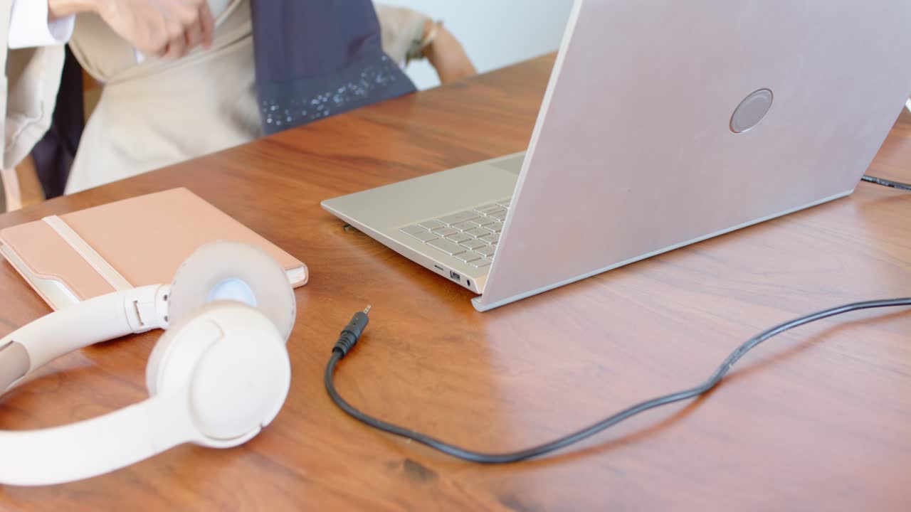 Donna che si avvicina a una sedia, seduta a una scrivania da lavoro, che indossa una sciarpa e collega un cavo al laptop per lavorare.