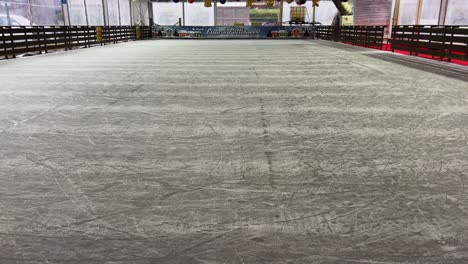 Empty-indoor-ice-rink-and-frozen-floor-for-skating-with-Christmas-decorations-hanging-on-ceiling