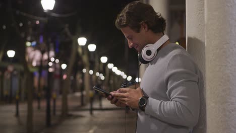 hombre caucásico con auriculares, bebiendo, usando su teléfono por la noche