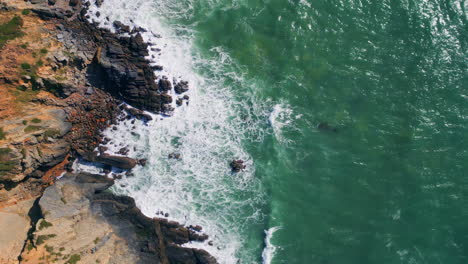 top view waves barrelling to rugged coastal cliffs. drone shot powerful ocean