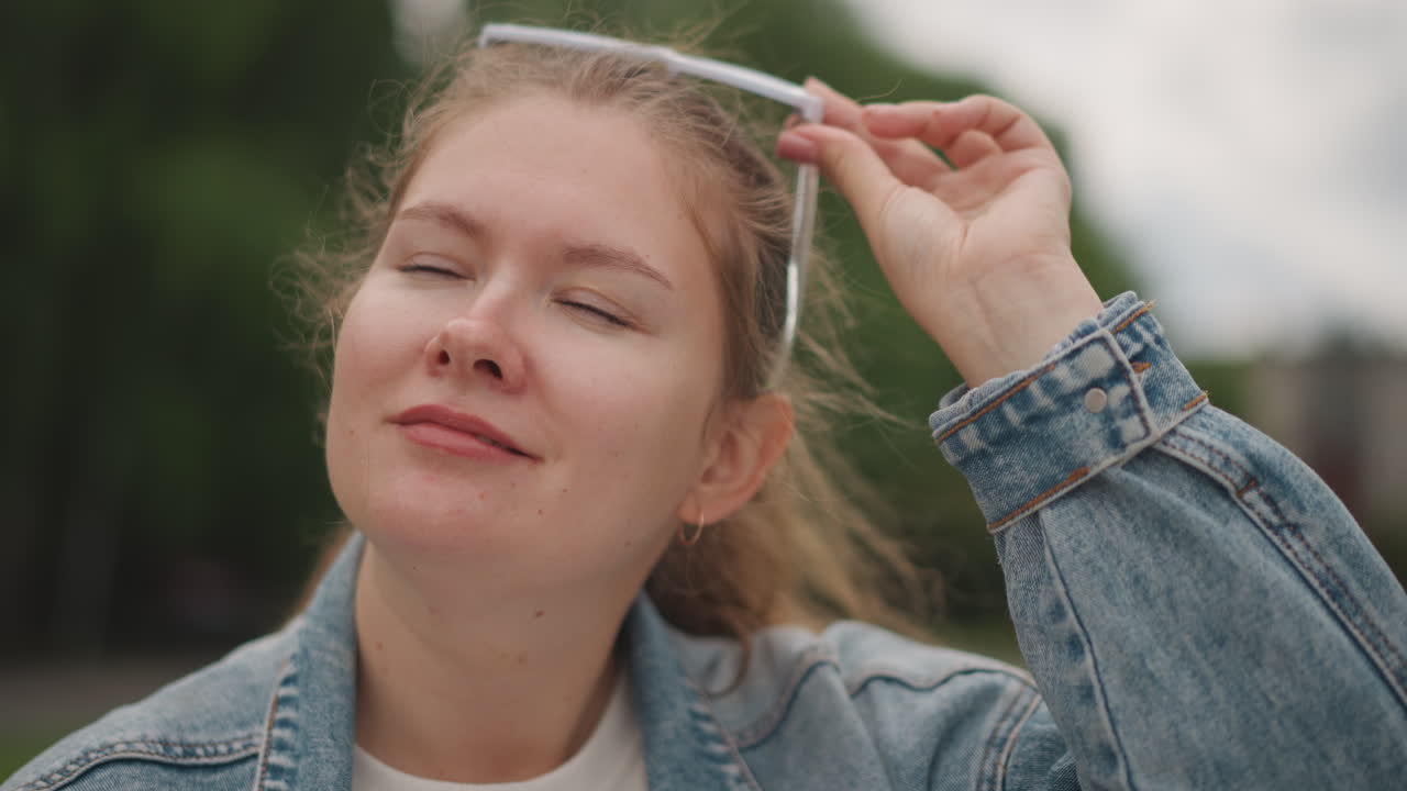 Ragazza felice che si rilassa. Studentessa che si rilassa in un parco soleggiato. Ragazza adolescente con occhiali da sole seduta pacificamente su una panchina. Giovane donna con gli occhi chiusi che sorride dolcemente in un luminoso ambiente di parco all'aperto.