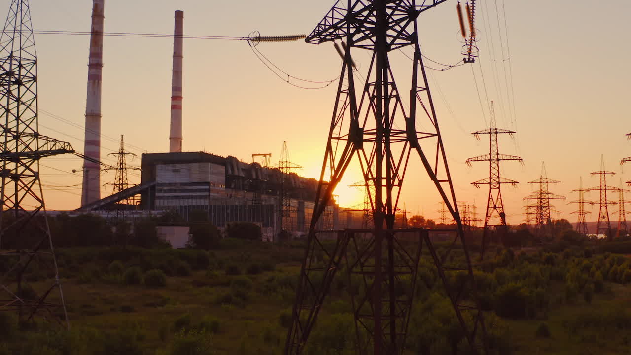 Tall voltage tower. Distribution and supply electricity at sunset. Power electric station with transmission lines against the orange sun. Camera rising up.