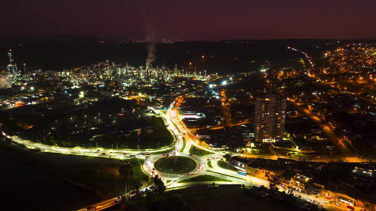 Hiperlapso aéreo del tráfico en la rotonda de Concón iluminada por la noche con humo de la refinería ENAP Aconcagua, Valparaíso, Chile