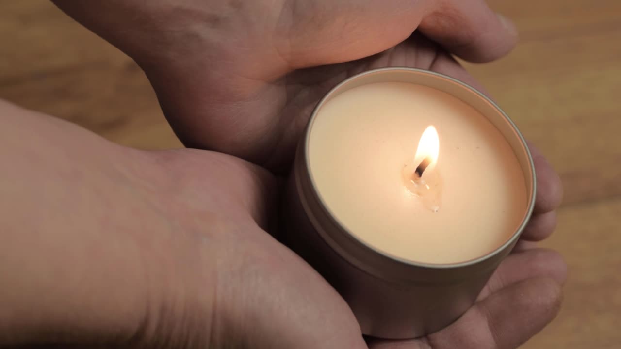 Two hands holding lit scented candle
