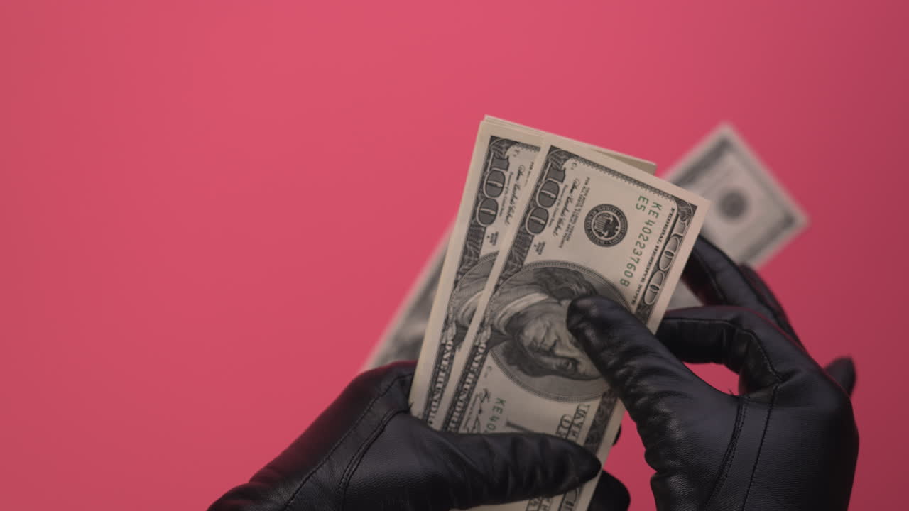 Gloved Hands Dropping Hundred Dollar Bills on Pink Background