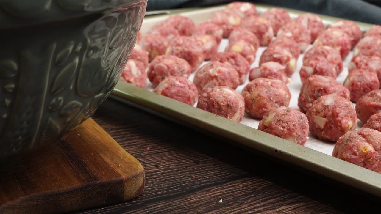 Close up of Italian meatballs being used in Italian Wedding Soup for dinner. Meatballs on a baking sheet sliding across the counter and going into the oven to bake. Lots of meatballs made with beef.