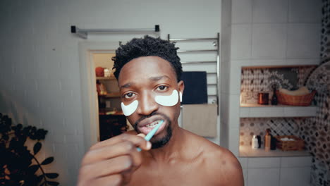 young black man with under-eye patches brushing teeth in bathroom at home