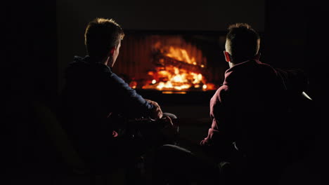 man plays guitar by the fireplace next to a friend