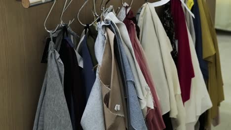 camera pan of colorful cloth scraps hanging on the side of a wooden table in metal hangers - shallow depth of field interior scene