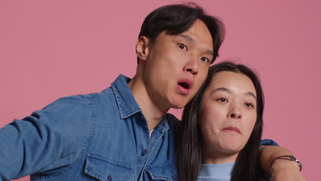 Young-Loving-Couple-In-Front-Of-Pink-Studio-Background-Having-Fun-Posing-For-Photo-Booth-Style-Portraits