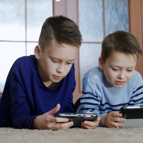 cute boys lying on the floor in the living-room and playing on modern devices with excited faces. children enjoying with their gadgets and showing interesting moments each other at home.