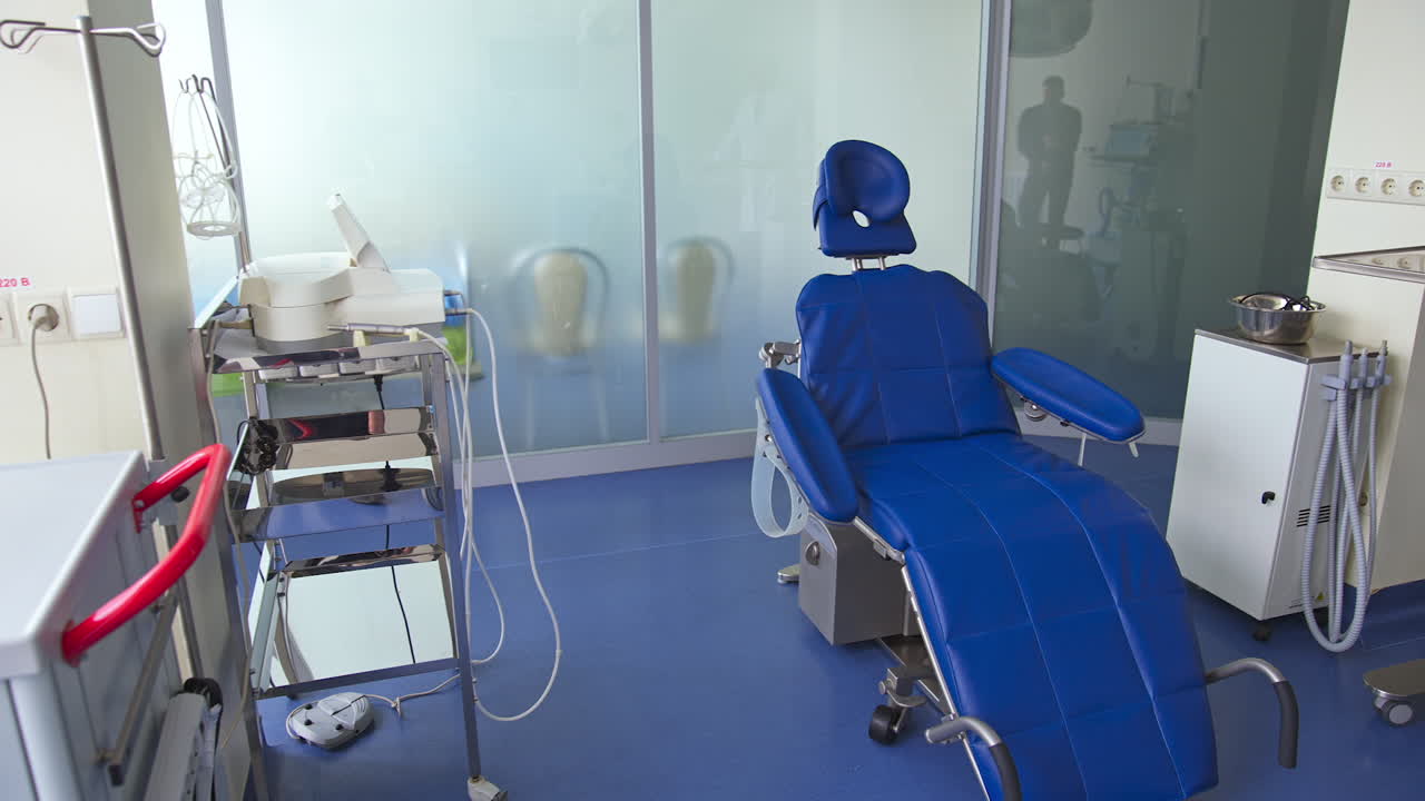 Blue comfortable folding chair in dentist's cabinet. Light room with diverse equipment for stomatological purposes.