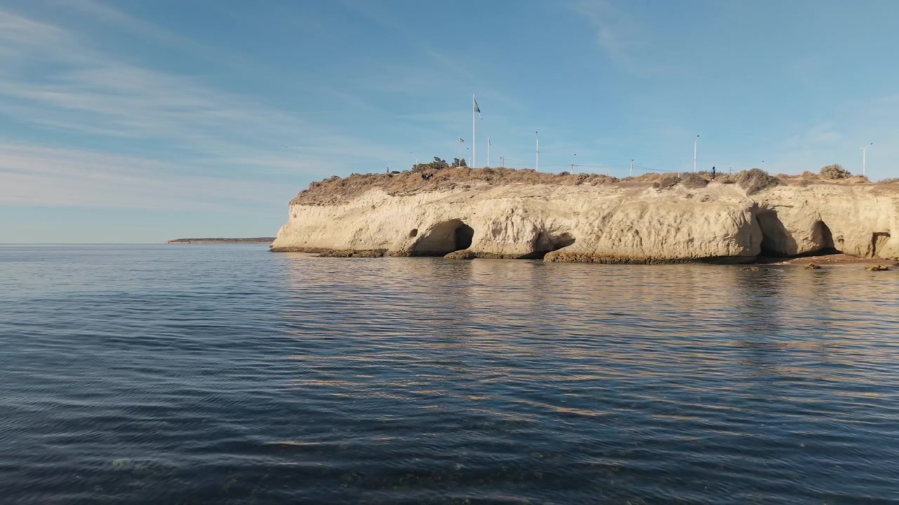 Droneopptak som glir langs steinete kystklipper og rolig atlanterhavsvann ved Punta Cuevas, Argentina.