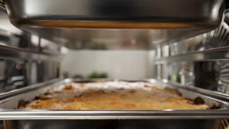 close-up of a professional kitchen's steel oven with a lasagna dish in focus, creating a warm, busy atmosphere