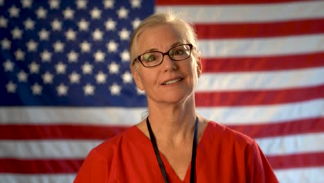 Medium-tight-portrait-of-a-healthcare-nurse-with-clipboard-looking-happy-and-relieved-with-an-out-of-focus-American-flag