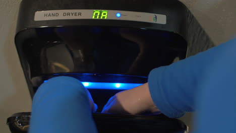 Close-up-view-of-woman-drying-hands-after-washing-in-modern-air-hand-dryer