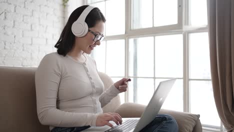 happy young asian woman doing payments online or shopping in internet store holding credit card using laptop computer