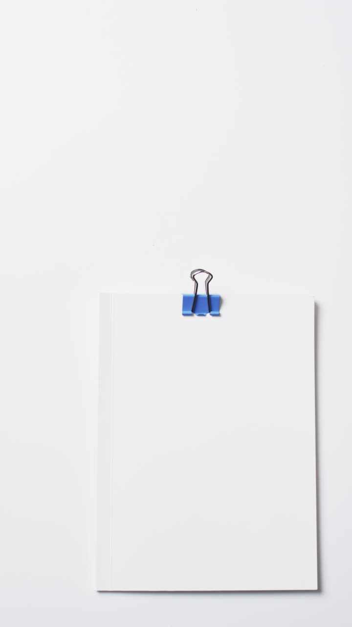 Vídeo de livros com páginas brancas em branco e clipe de papel azul com espaço para texto em fundo branco.