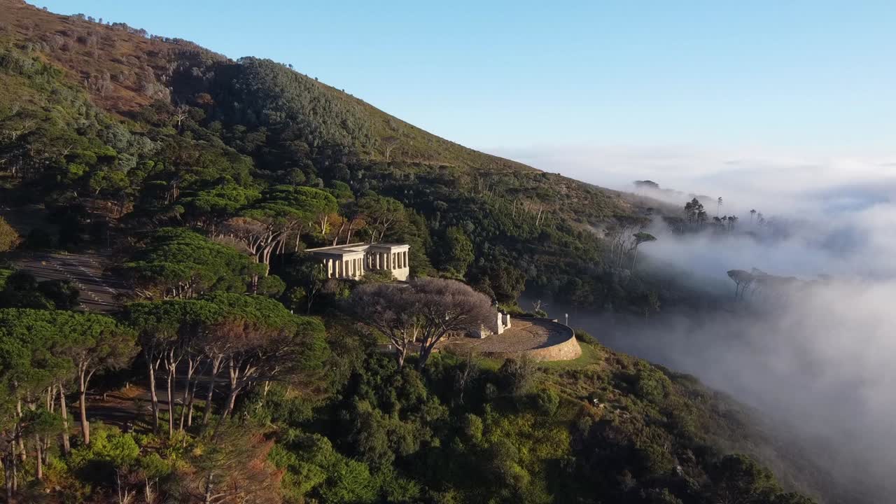 A building nestled on a forested mountainside with a valley of clouds below
